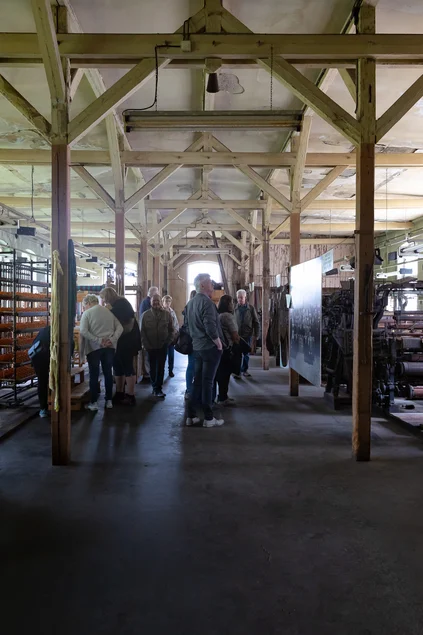 In der Schärerei In einem großen Maschinensaal steht eine Gruppe Menschen, die diverse historische Maschinen betrachten.