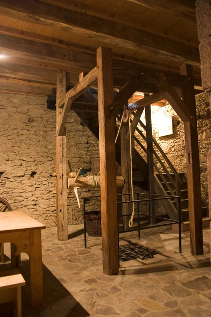 Folterkammer Blick in ein Verlies mit Natursteinwänden mit einer hölzernen Balkenvorrichtung, die über eine Seilwinde verfügt. Das Seil hängt über einem Eisengitter im Fußboden, unter dem sich ein weiterer Kellerraum befindet.