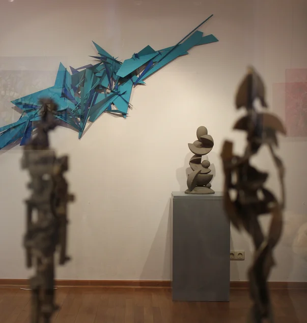 Abstrakte Skulpturen sind vor einer Wand mit einem ebenfalls abstrakten Werk angeordnet.