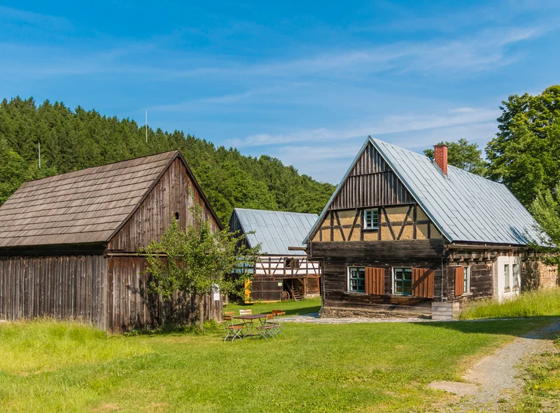 Historisches Bauernhof-Ensemble, bestehend aus zwei Fachwerkhäusern und einer Holzscheune, davor ein Tisch mit Stühlen