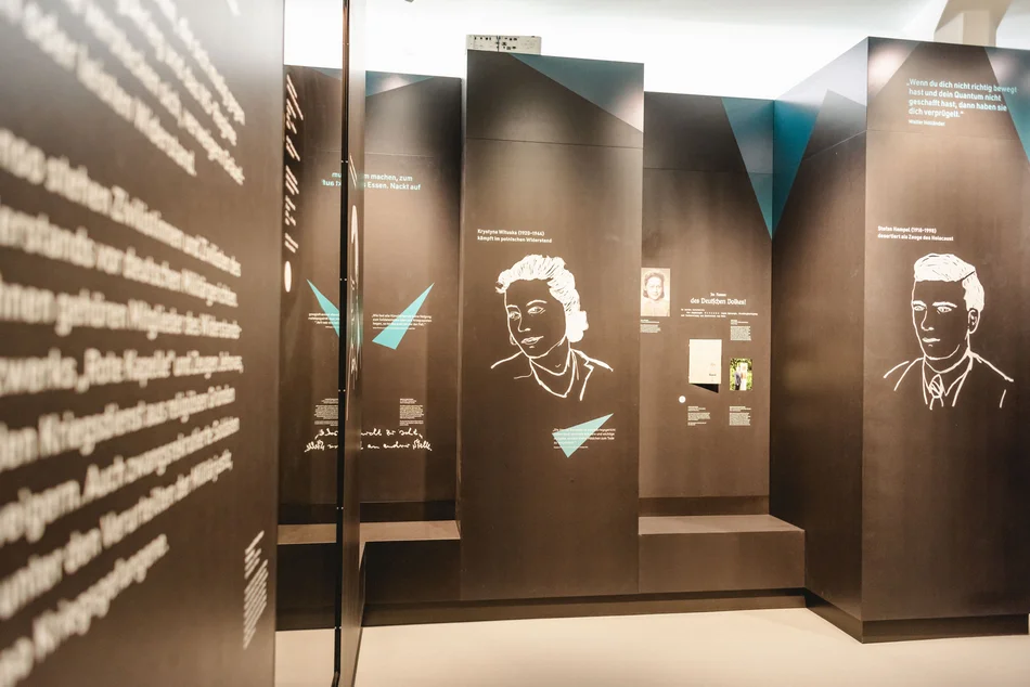 Blick in ein in Dunkelgrau gehaltenes Ausstellungsmodul, an dessen Wände Texte und Bilder aufgebracht sind