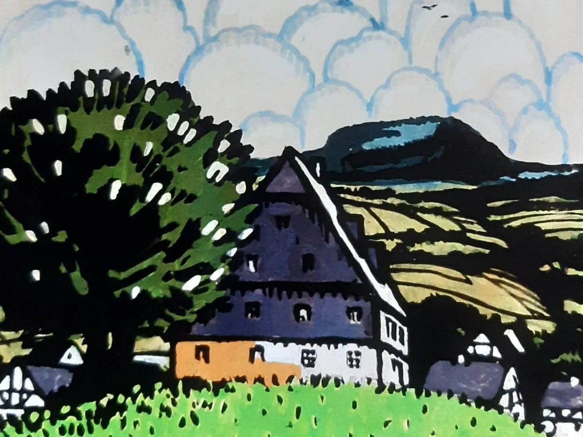 Ein Haus mit dominantem, in grauem Schiefer gedeckten Spitzdach in erzgebirgischer Landschaft, davor eine blühende Kastanie