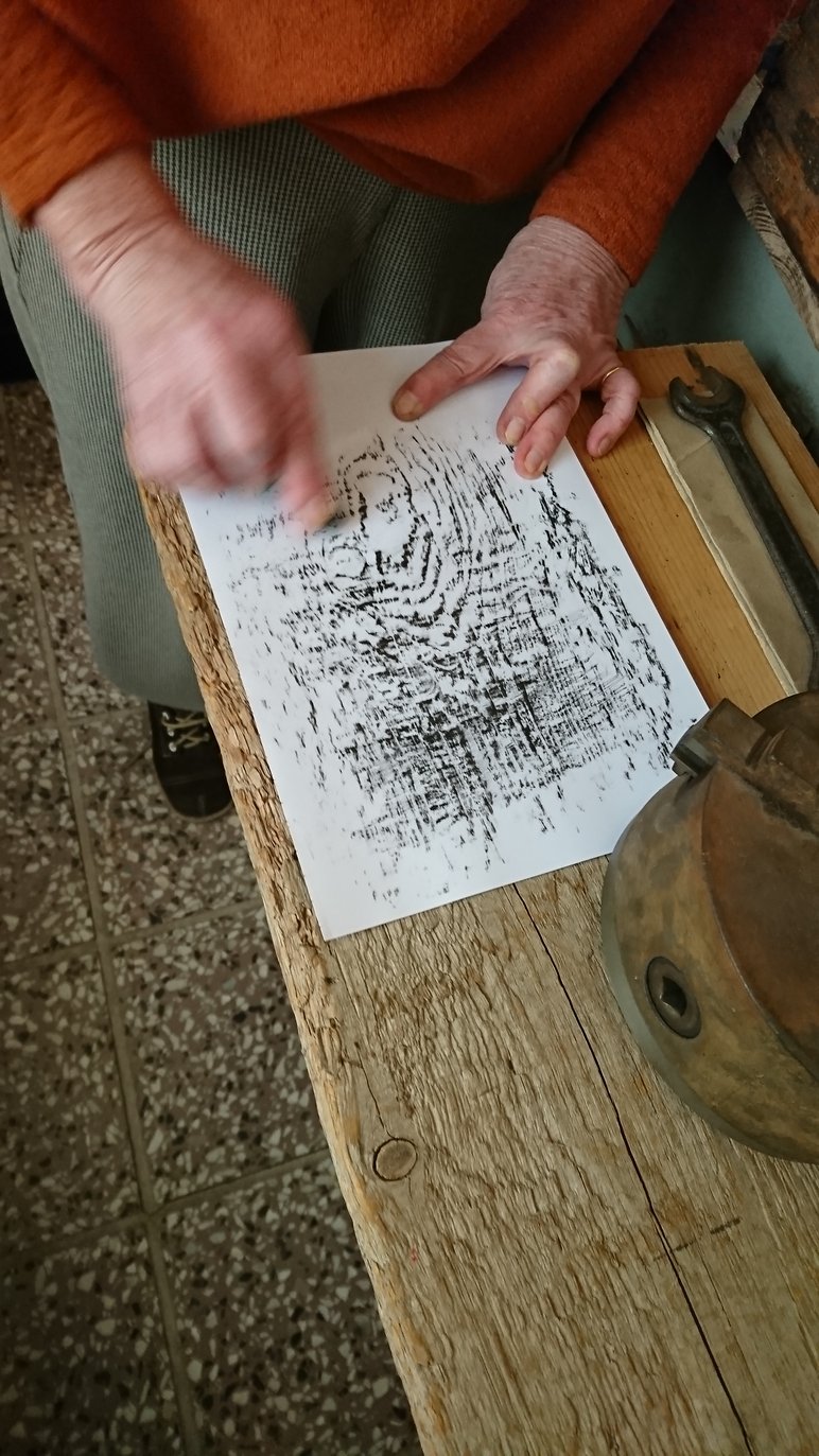 Das Foto zeigt, wie eine Handwerkerin mit Druckertinte die Struktur eines darunterliegenden Holzes auf Papier überträgt.
