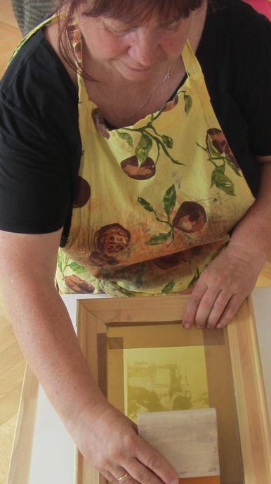 Siebdruck Eine Frau stellt mit einem Sieb einen farbigen Druck auf Papier hier.