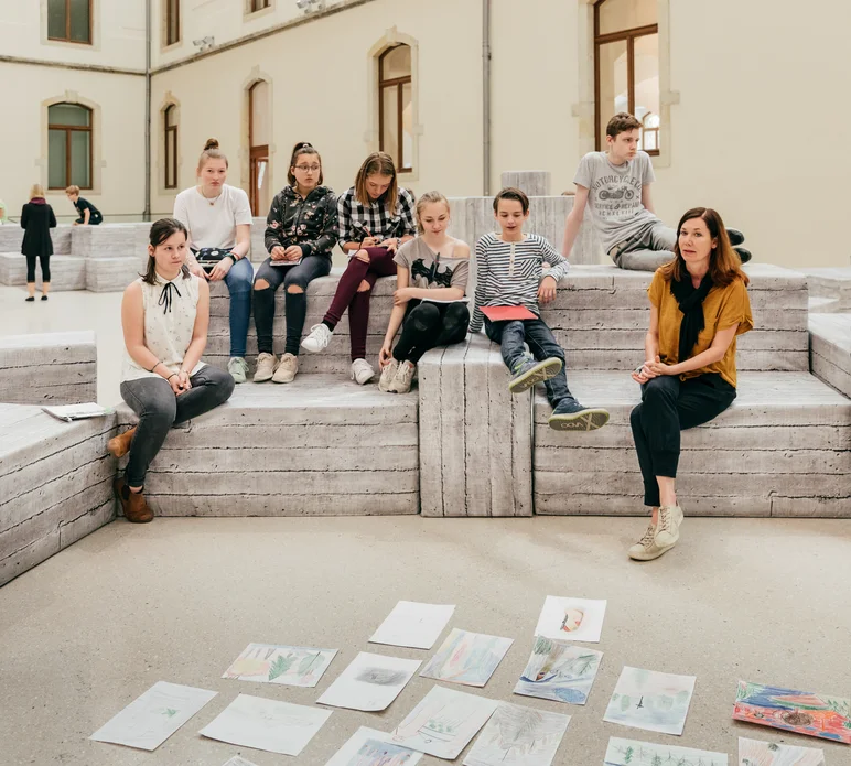 Das Foto zeigt mehrere Schülerinnen und Schüler und zwei Kunstvermittlerinnen auf den Sitzmöbeln im Lichthof des Dresdener Albertinums sitzend.