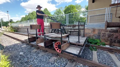 Ein Mann steht auf einer Draisine, einem sich auf Schienen bewegenden Gefährt aus Stahl und Holz.