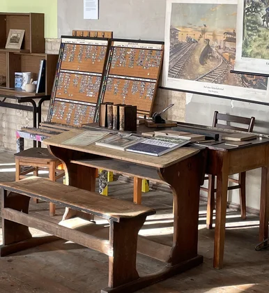 Blick in ein historisches Klassenzimmer mit alten Schulbänken sowie historischen Büchern und Anschauungstafeln