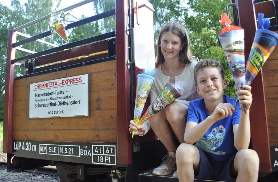 Zuckertüten-Express im Chemnitztal Ein Mädchen und ein Junge sitzen im Einstiegsbereich eines offenen Eisenbahnwaggons und halten je zwei kleine Zuckertüten in den Händen.
