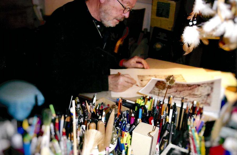 Dieses Bild zeigt Thomas Michael Ranft sitzend am Arbeitstisch im Atelier, zu sehen sind auch Gefäße mit Stiften und Pinseln.