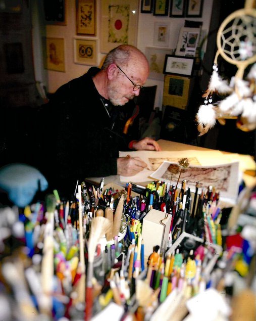Dieses Bild zeigt Thomas Michael Ranft sitzend am Arbeitstisch im Atelier, zu sehen sind auch Gefäße mit Stiften und Pinseln.