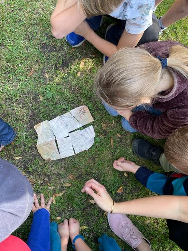 Schatzsuche Nahaufnahme einer von oben fotografierten Kindergruppe, die sich über eine aus Teilstücken zusammengesetzte Schatzkarte beugt
