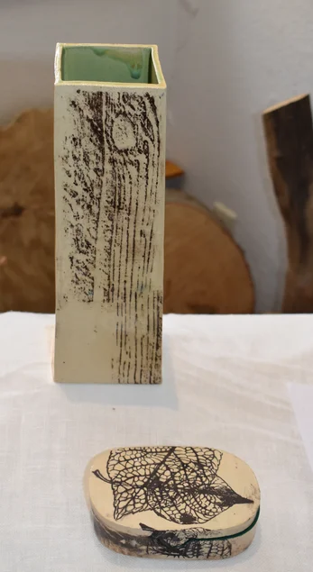 Zwei weiße Keramiken mit schwarzen Strichmustern, die einerseits an Holz und andererseits an Blätter erinnern