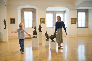 Ein großes und ein kleines Kind in einem weitläufigen Ausstellungsraum mit Skulpturen verschiedener Tiere