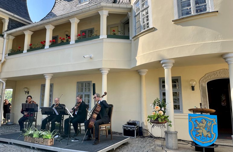 Eine Musikerin und drei Musiker spielen Violine, Bratsche und Cello auf einer im Innenhof eines historischen Gebäudes aufgestellten Bühne.