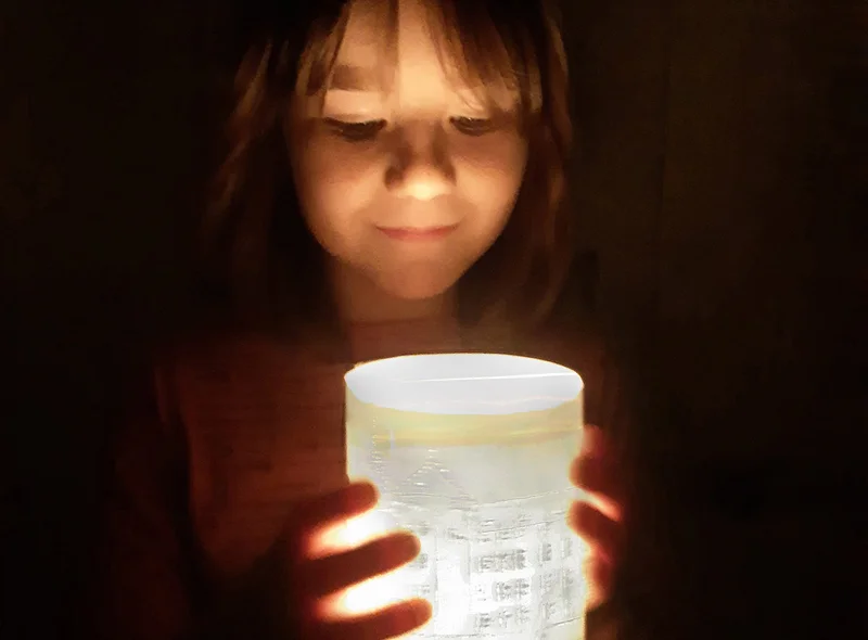 Ein Mädchen (circa 7 Jahre) blickt auf ein selbst gebasteltes Windlicht, auf dem Schloss Hartenfels abgebildet ist.