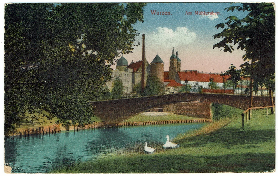 Historische, kolorierte Postkarte, die einen Flusslauf mit Steinbrücke und im Hintergrund die Dächer und Türme einer Stadt zeigt