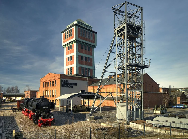 Foto eines Klinker-Ensembles mit Förderturm und sich anschließenden niedrigeren Industriebauten, daneben steht ein weiterer, aus Stahl konstruierter Turm.