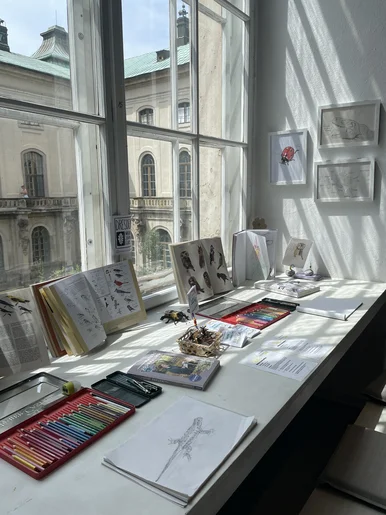 Auf einer Fensterbank sind Skizzenhefte und Zeichenmaterialien ausgebreitet.