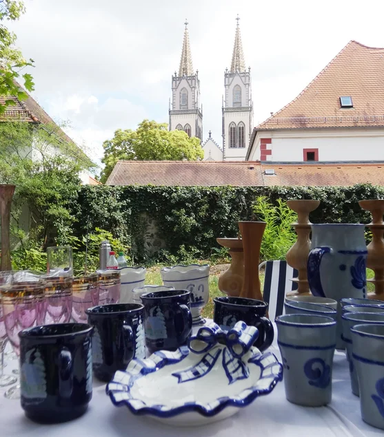 Keramik und Gläser auf einem Tisch im Freien, im Hintergrund die Türme einer Kirche