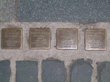 Das Foto zeigt vier quadratische, kupferfarbene Steine, die in einen kopfsteingepflasterten Gehweg eingelassen sind. Auf diesen sogenannten Stolpersteinen stehen die Namen der Opfer, ihr Geburtsjahr und wie sie gestorben sind – in diesem Fall erinnern sie an die Familie Grossmann in Bautzen.