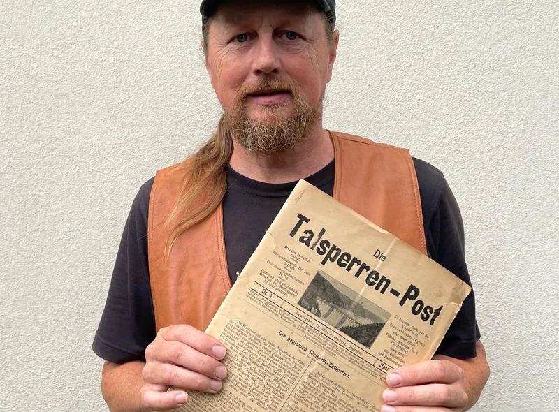 Eckhart Böhm, ein Mann mittleren Alters mit Kappe und Zopf, hält die historische Zeitschrift Die Talsperren-Post in der Hand