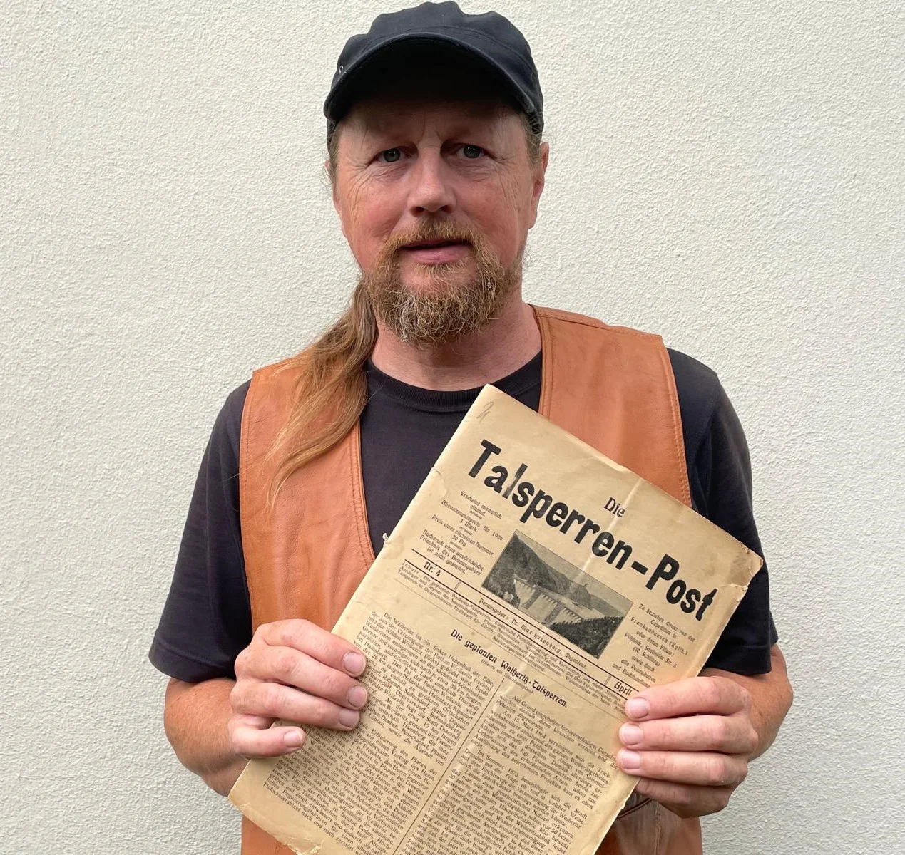 Eckhart Böhm, ein Mann mittleren Alters mit Kappe und Zopf, hält die historische Zeitschrift Die Talsperren-Post in der Hand