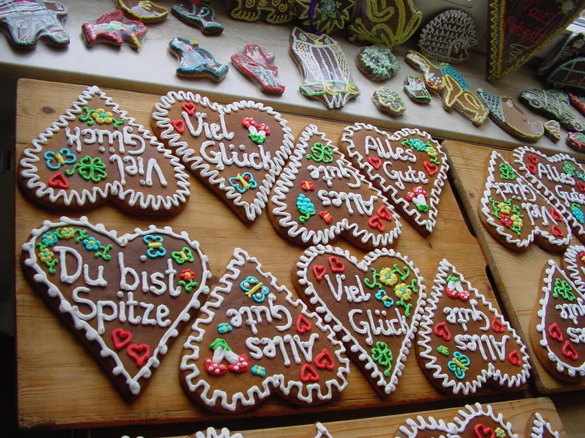 Auf mehreren Holzbrettern liegen bunt verzierte Pfefferkuchenherzen, die mit Sprüchen wie "Du bist Spitze", "Alles Gute" und "Viel Glück" versehen sind.