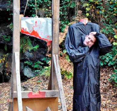 Neben der Attrappe einer mit roter Farbe beschmierten Guillotine steht eine mannshohe Puppe die ihren Kopf in den Händen hält