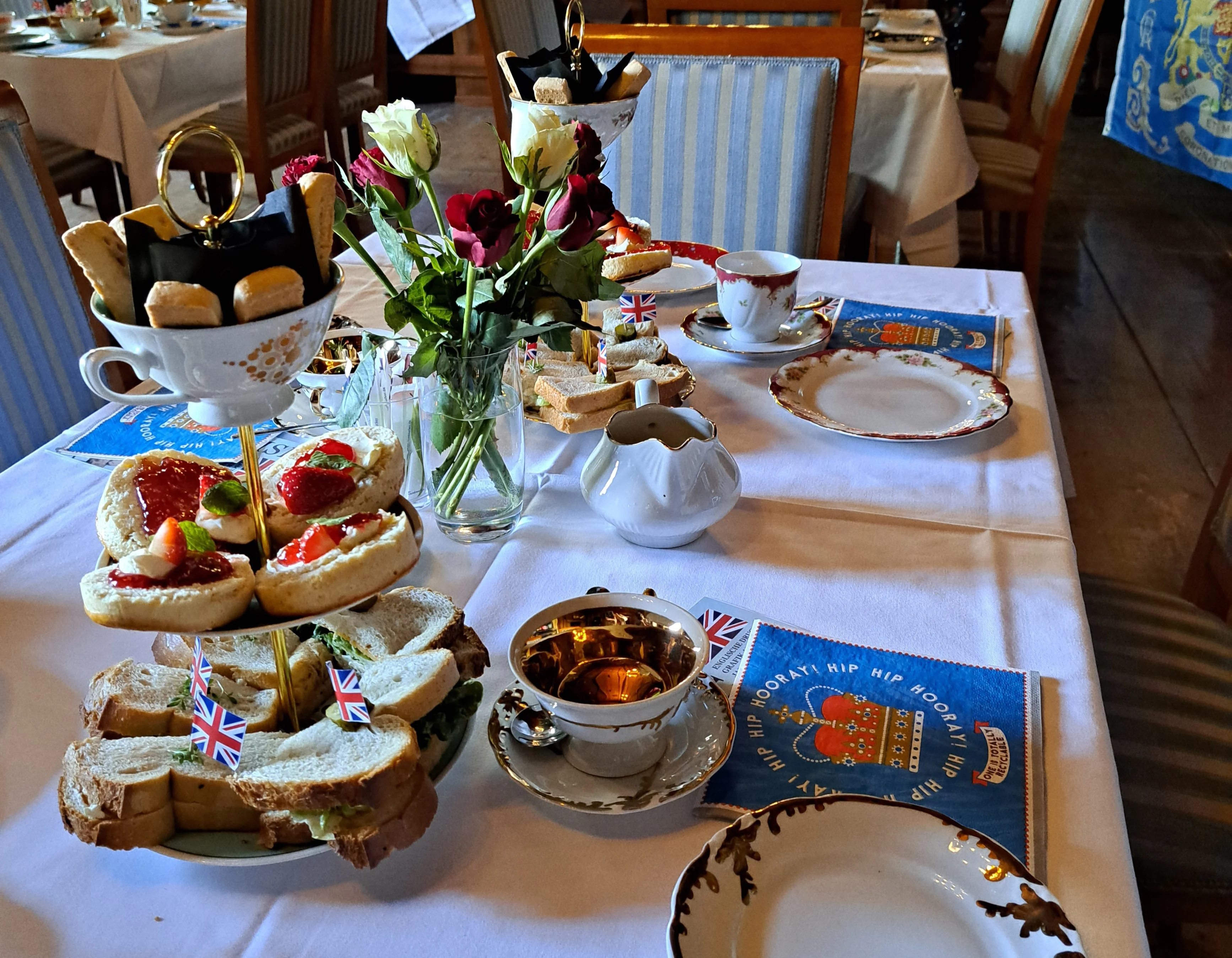 Das Foto zeigt einen hübsch eingedeckten Tisch mit Sammeltassen, Etagere, Servietten und Blumen für eine englische Tea Time.