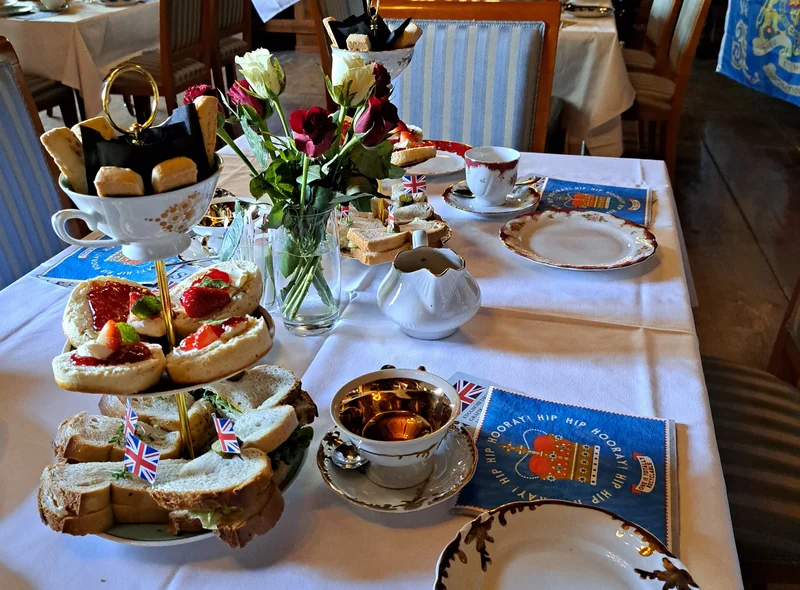 Das Foto zeigt einen hübsch eingedeckten Tisch mit Sammeltassen, Etagere, Servietten und Blumen für eine englische Tea Time.