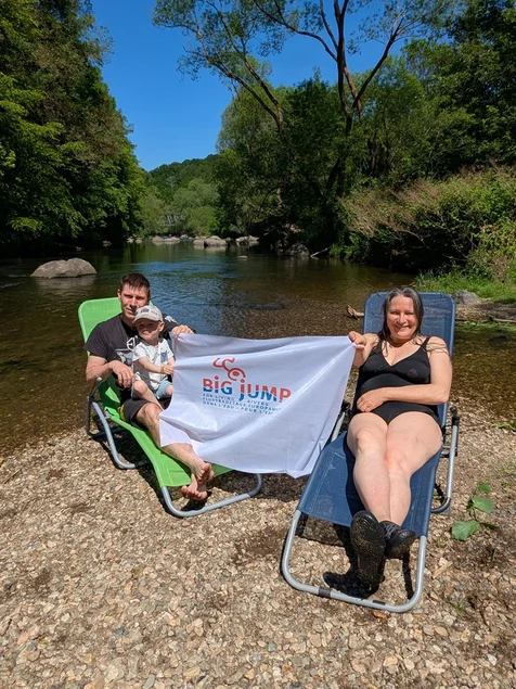Zwei Personen mit Sonnenliegen auf Insel im Fluss mit Werbebanner für den Flussbadetag