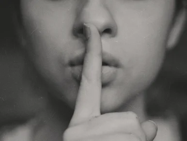 Das Bild zeigt die Nahaufnahme einer Person, die ihren Finger vor ihren Mund hält.
