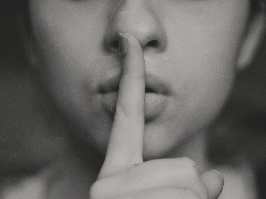 Das Bild zeigt die Nahaufnahme einer Person, die ihren Finger vor ihren Mund hält.