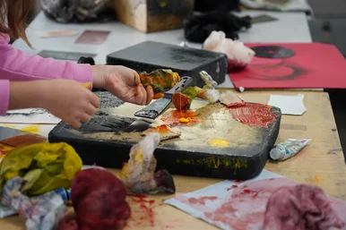 Auf eine mit Einkerbung versehene Steinplatte streicht ein Kind verschieden farbige Pasten.