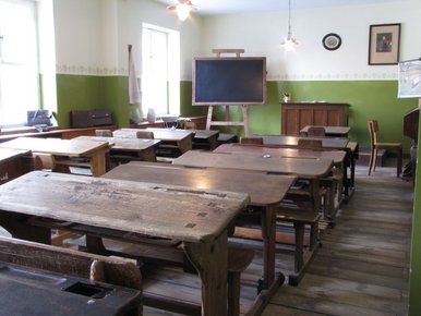 Foto der Inszenierung eines Klassenzimmers um 1900, mit mehreren hölzernen Schulbänken und einer alten Tafel