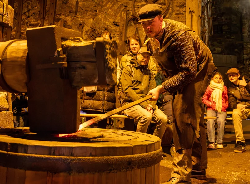 Vor einer Besuchergruppe führt ein Mann im historischen Frohnauer Hammer das Schmieden vor.