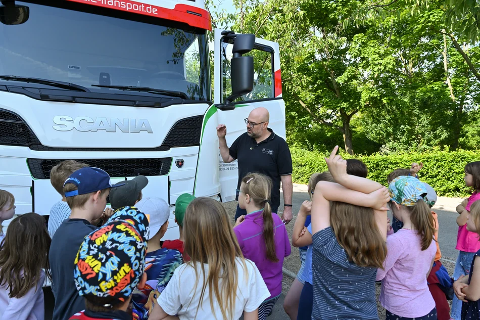Lkw-Sicherheitsvorführung Gruppe von Kindern steht vor einem Lkw mit geöffneter Tür, davor ein Mann, der etwas erklärt.