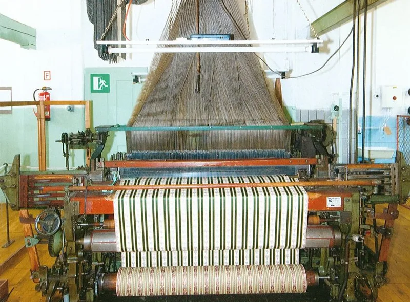 Historische, über Lochbänder gesteuerte Maschine, die aus einer Unzahl einzelner Fäden einen grün-weiß-gestreiften Stoff webt