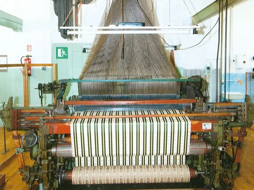 Jacquardwebmaschine Historische, über Lochbänder gesteuerte Maschine, die aus einer Unzahl einzelner Fäden einen grün-weiß-gestreiften Stoff webt