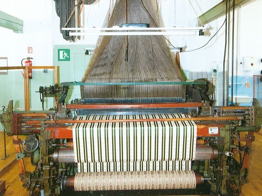 Historische, über Lochbänder gesteuerte Maschine, die aus einer Unzahl einzelner Fäden einen grün-weiß-gestreiften Stoff webt