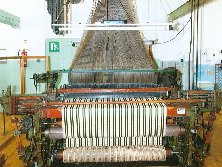 Historische, über Lochbänder gesteuerte Maschine, die aus einer Unzahl einzelner Fäden einen grün-weiß-gestreiften Stoff webt