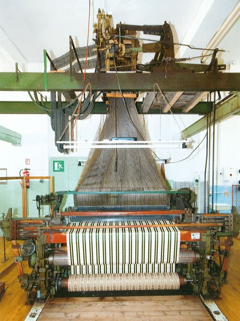 Historische, über Lochbänder gesteuerte Maschine, die aus einer Unzahl einzelner Fäden einen grün-weiß-gestreiften Stoff webt