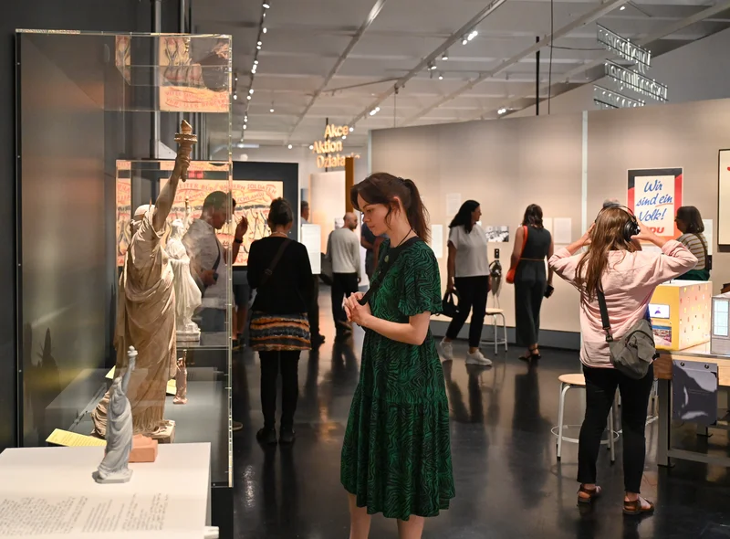 Eine Besucherin betrachtet ein Modell der Freiheitsstatue. Im Hintergrund schauen sich Menschen weitere Exponate an.