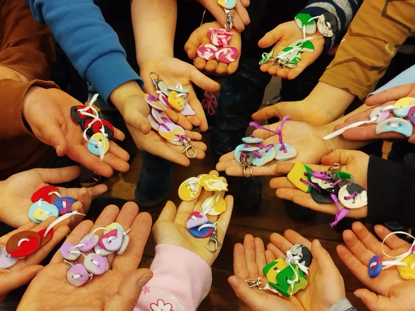 Hier könnt ihr Knöpfe selbst herstellen und die Geschichte der Posamenten in Marienberg kennenlernen. Viele Kinderhände formen einen Kreis und zeigen selbstgefertigte Knöpfe.