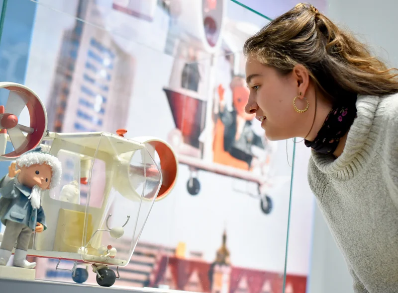 Das Foto zeigt ein Objekt der Ausstellung. Eine Besucherin schaut auf das kleine Flugmodell mit dem Sandmann.