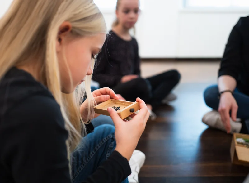 Kinder betrachten ein kleines Kästchen mit gebläuten Schrauben aus einer Armbanduhr