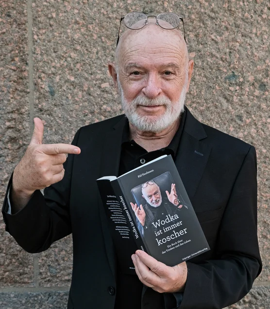 Porträtfoto eines grauhaarigen Mannes mit Brille und Bart, der mit einer Hand das Buch „Wodka ist immer koscher“ hält und mit der anderen Hand darauf zeigt