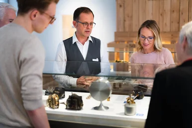 Ein Mann zeigt Museumsgästen historische Zeitmesser in einer Ausstellungsvitrine.