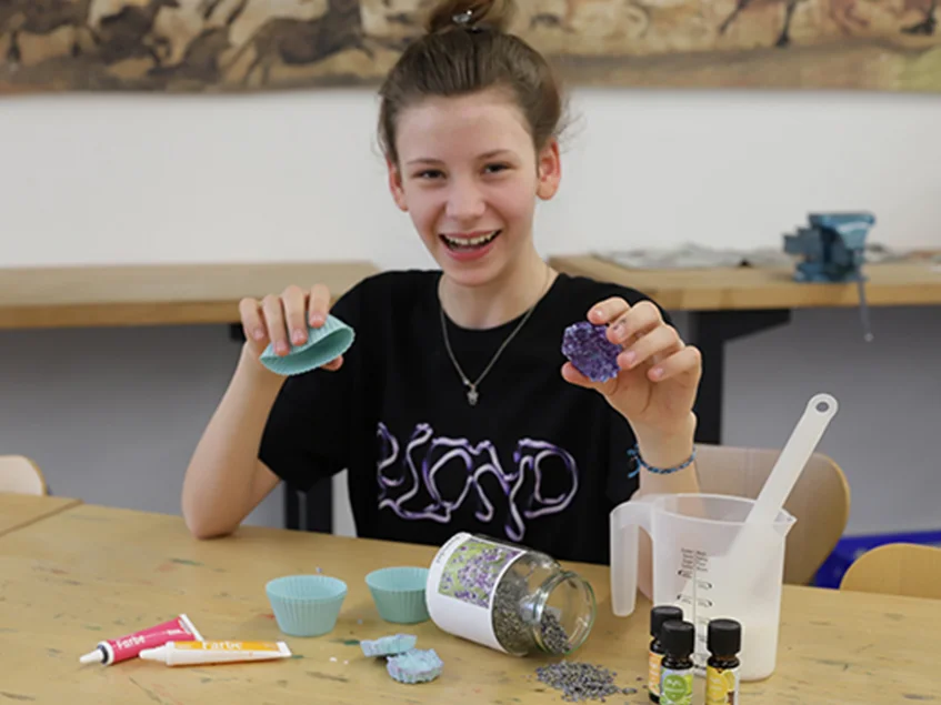 Sommerferienprogramm „Archäologie mit Wasser und Seife“ Das Bild zeigt ein Mädchen an einem Tisch. Sie hält Seife in den Händen.