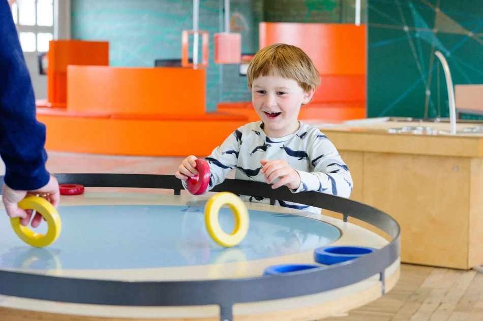 Ein fasziniertes Kind steht an einem Experimentiertisch mit verschiedenfarbigen Ringen zum Rollen.